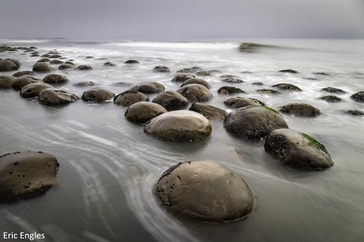 Photo of round rocks on the beach with an incoming tide in the background.